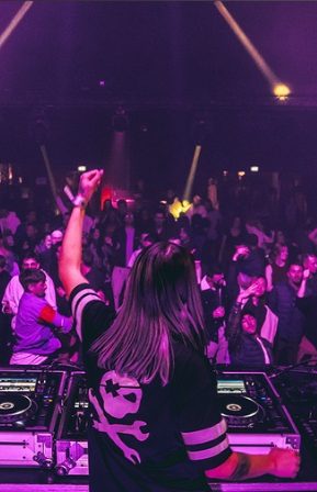 DJ en performance devant une foule dansante avec des lumières colorées.